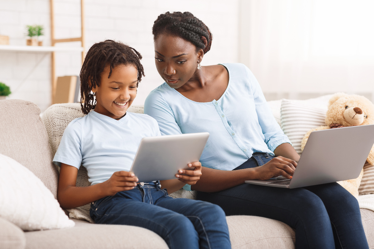 Mother and child using tablet and laptop on sofa
